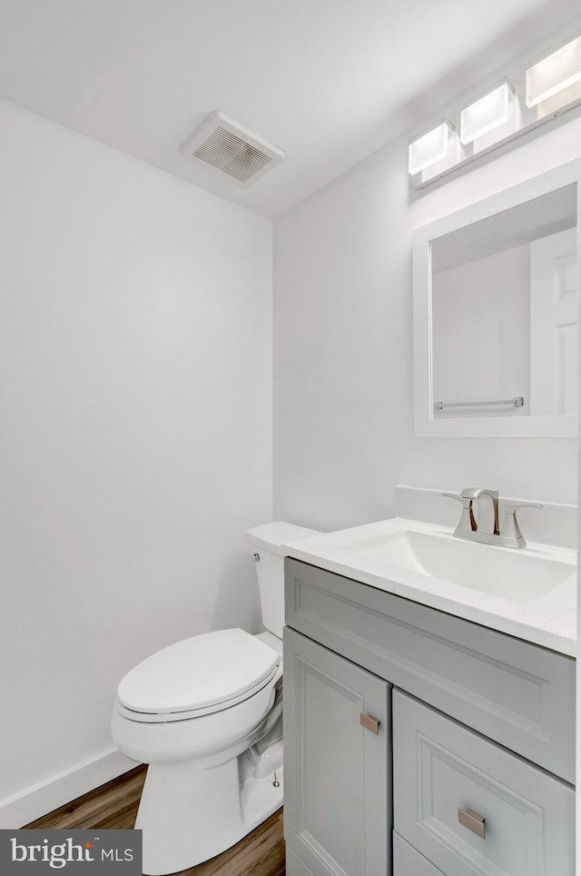 half bath featuring wood finished floors, vanity, baseboards, toilet, and visible vents