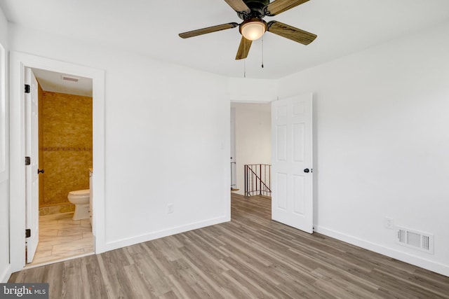unfurnished bedroom featuring baseboards, wood finished floors, visible vents, and ensuite bathroom