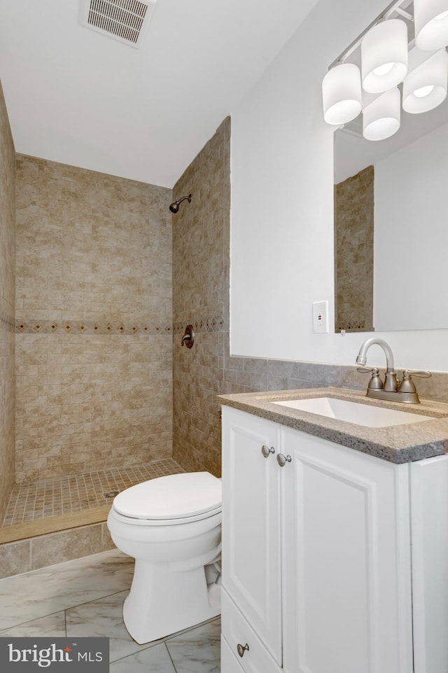 bathroom featuring a tile shower, marble finish floor, visible vents, toilet, and vanity
