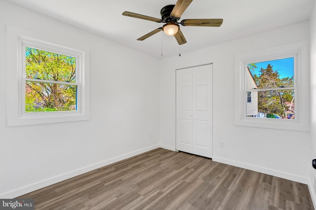 unfurnished bedroom featuring baseboards, wood finished floors, a closet, and multiple windows
