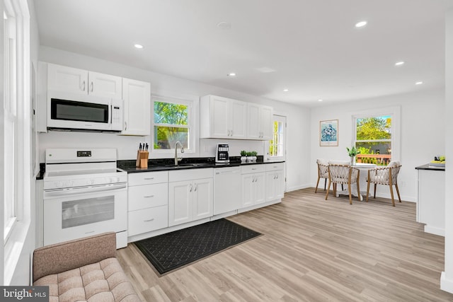 kitchen featuring a sink, light wood-type flooring, dark countertops, white cabinetry, and white appliances