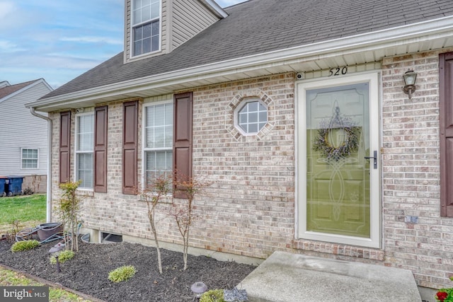 doorway to property with roof with shingles and brick siding