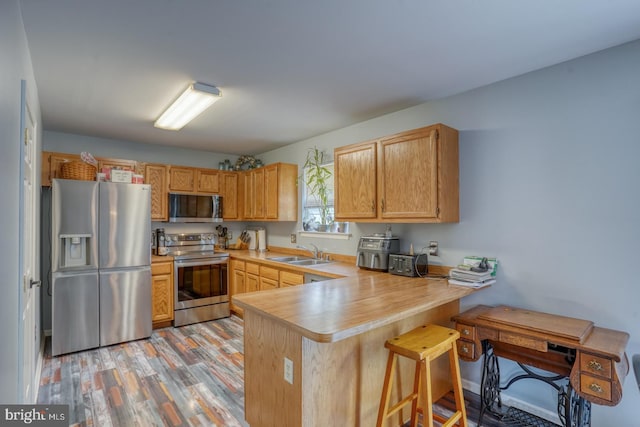 kitchen featuring appliances with stainless steel finishes, a sink, light countertops, a peninsula, and light wood-style flooring