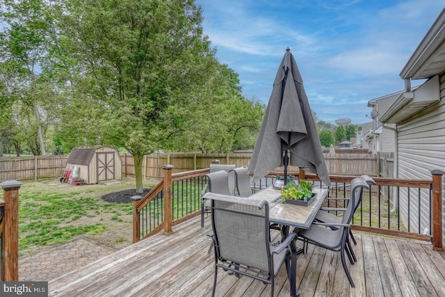 wooden terrace featuring an outdoor structure, outdoor dining area, a fenced backyard, a storage unit, and a lawn