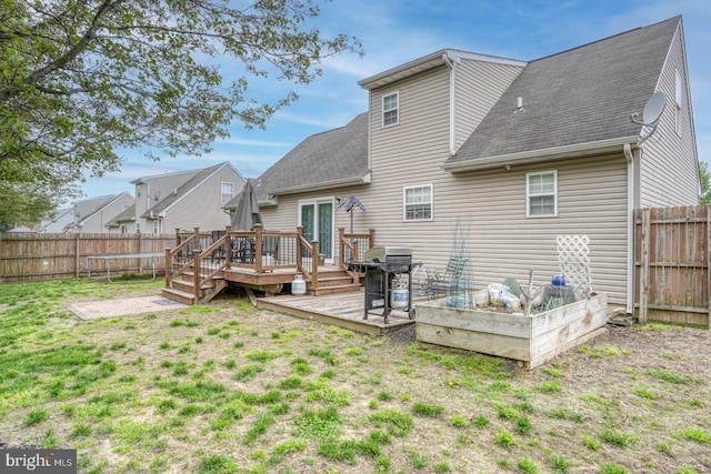 rear view of house featuring a deck, a fenced backyard, a vegetable garden, a shingled roof, and a lawn