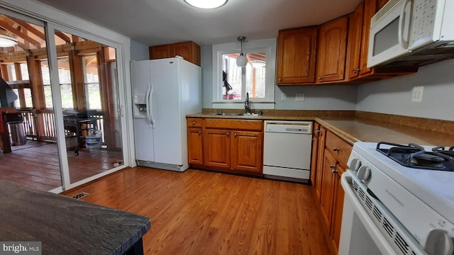 kitchen featuring brown cabinetry, a sink, white appliances, and light wood-style flooring
