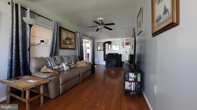 living area featuring baseboards, a ceiling fan, a wood stove, and dark wood-type flooring
