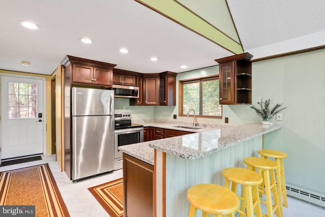 kitchen featuring light stone countertops, a sink, a peninsula, baseboard heating, and appliances with stainless steel finishes