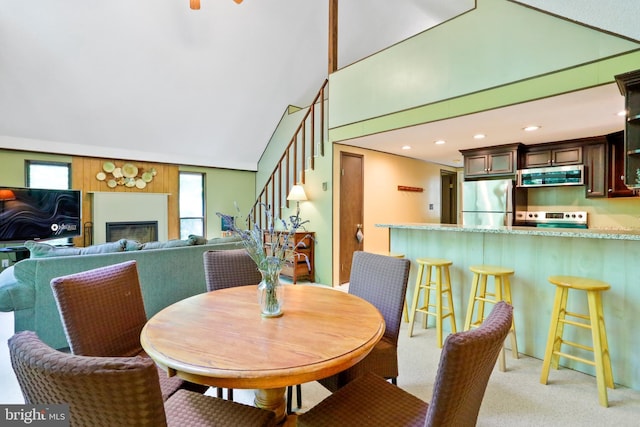 dining space with recessed lighting, stairs, light colored carpet, a glass covered fireplace, and a towering ceiling