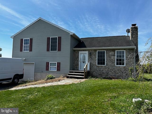 tri-level home featuring a chimney, a front yard, stone siding, and an attached garage