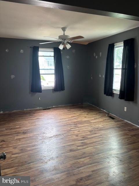 unfurnished room featuring baseboards, a ceiling fan, wood finished floors, and a healthy amount of sunlight