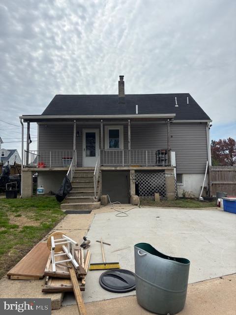 back of house with stairway, a porch, a patio area, an attached garage, and a chimney