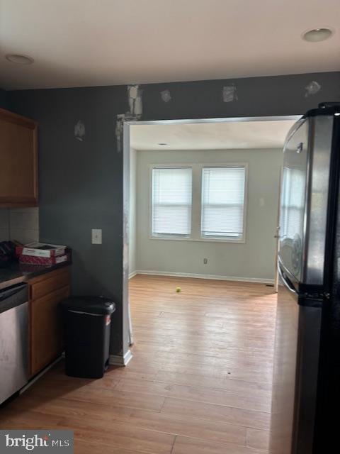 kitchen with baseboards, dark countertops, freestanding refrigerator, light wood-style floors, and stainless steel dishwasher