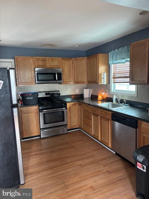 kitchen featuring light wood-style flooring, appliances with stainless steel finishes, a sink, dark countertops, and backsplash