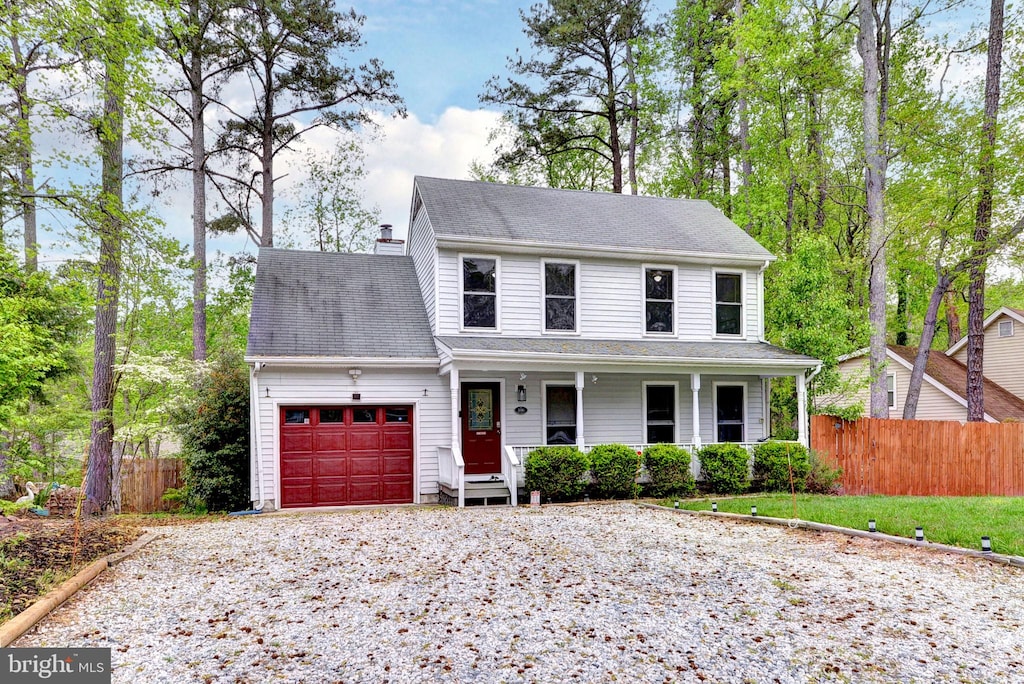 view of front of house with covered porch, an attached garage, gravel driveway, and fence