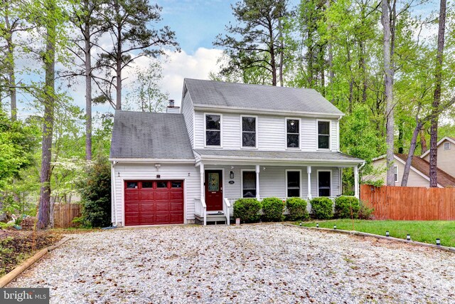 view of front of house with covered porch, an attached garage, gravel driveway, and fence