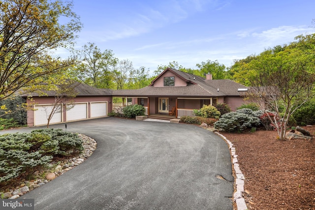 view of front of home featuring driveway, a chimney, roof with shingles, covered porch, and a garage