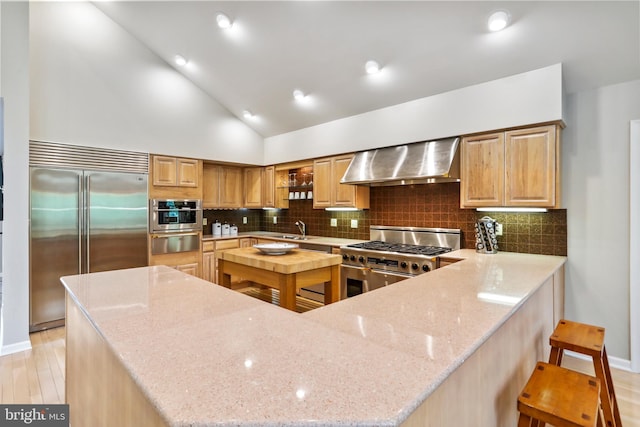 kitchen with a sink, a warming drawer, wall chimney exhaust hood, high quality appliances, and a peninsula