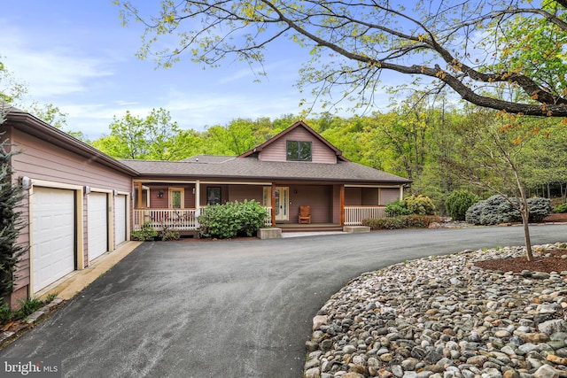 view of front facade featuring driveway, covered porch, a shingled roof, and an attached garage