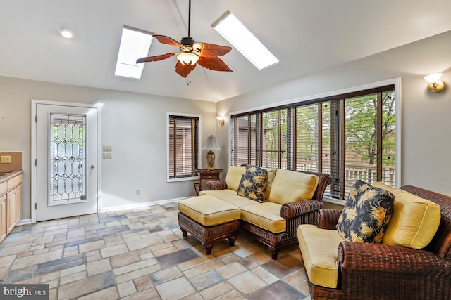 living room with lofted ceiling with skylight, ceiling fan, baseboards, and stone tile flooring