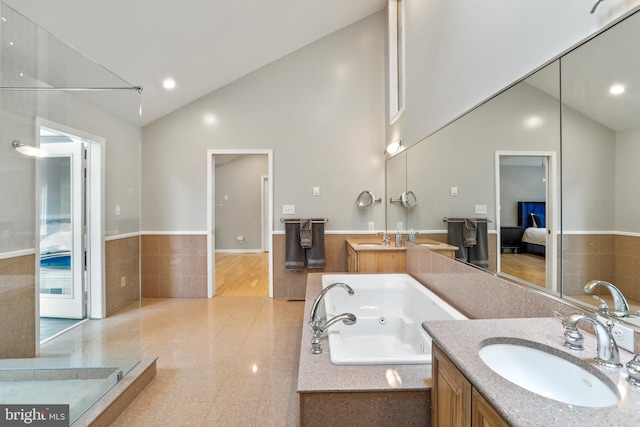 ensuite bathroom featuring high vaulted ceiling, two vanities, a whirlpool tub, and a sink