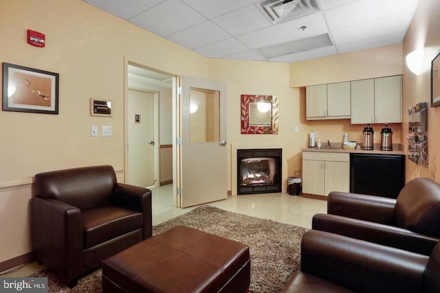 living area featuring visible vents, baseboards, a drop ceiling, and a glass covered fireplace