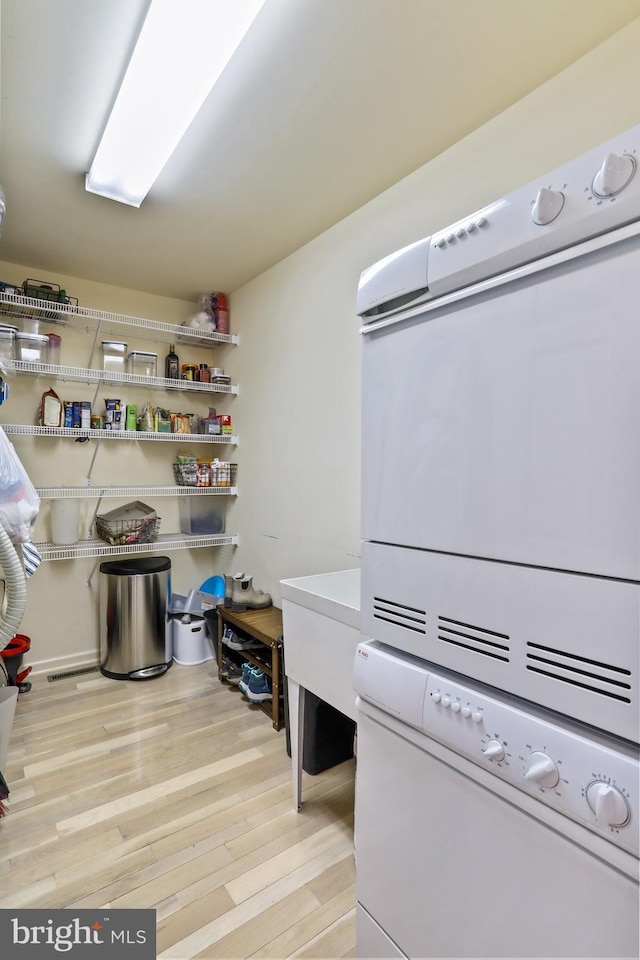 laundry room with wood finished floors, stacked washer / drying machine, and laundry area