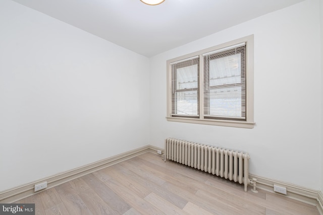 spare room with baseboards, radiator heating unit, and light wood-style floors
