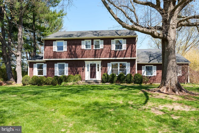 colonial house featuring a shingled roof and a front lawn
