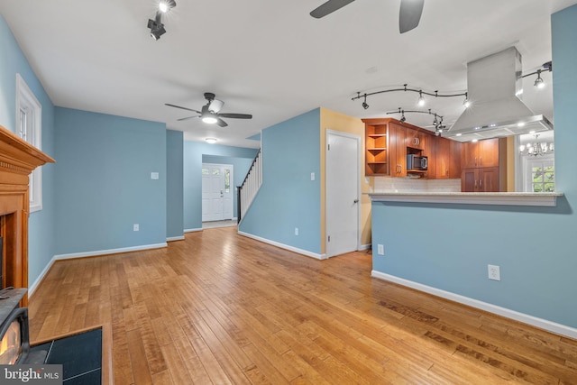 unfurnished living room with light wood-style floors, ceiling fan with notable chandelier, baseboards, and rail lighting
