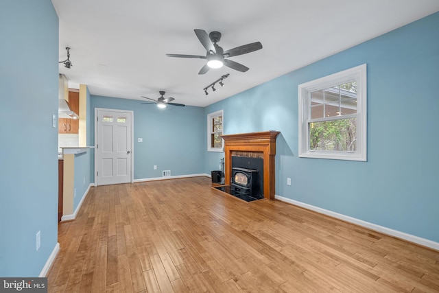 unfurnished living room with light wood-type flooring, rail lighting, a wood stove, visible vents, and ceiling fan