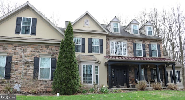 view of front of property with covered porch, a front yard, stone siding, and stucco siding