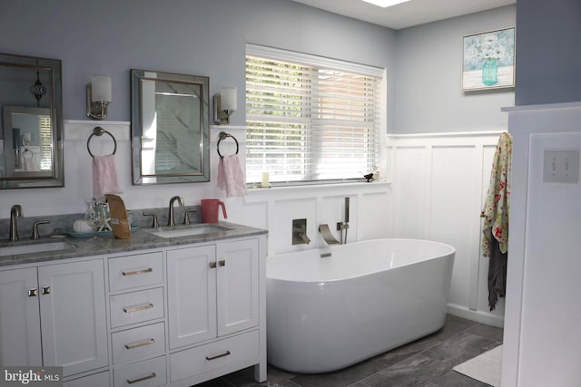 bathroom with a wainscoted wall, a freestanding tub, a sink, and a decorative wall