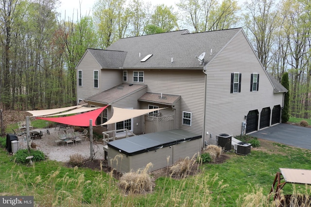 rear view of property featuring an attached garage, driveway, a shingled roof, and cooling unit