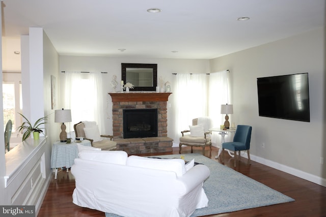 living room with a stone fireplace, dark wood-style flooring, and a healthy amount of sunlight