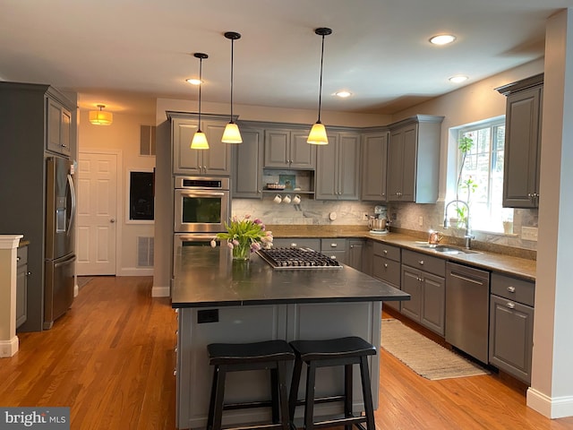 kitchen with gray cabinets, tasteful backsplash, a sink, light wood finished floors, and appliances with stainless steel finishes