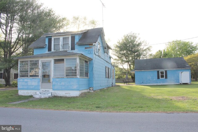 view of front of home featuring a shingled roof, a sunroom, and a front lawn