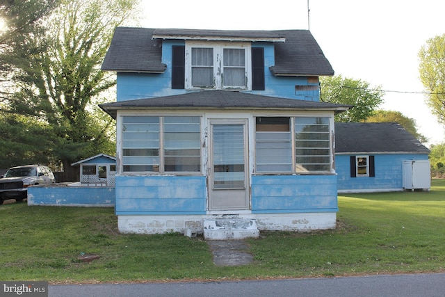 view of front facade with a shingled roof, a sunroom, and a front lawn