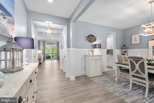 interior space featuring wainscoting, an inviting chandelier, light wood finished floors, and a decorative wall