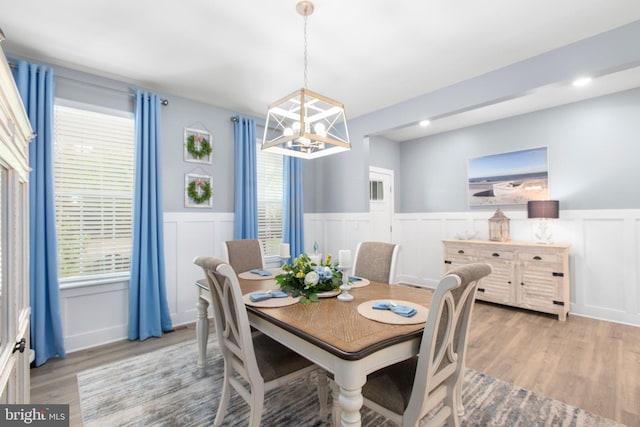 dining space with a wainscoted wall, a healthy amount of sunlight, an inviting chandelier, light wood-style floors, and a decorative wall