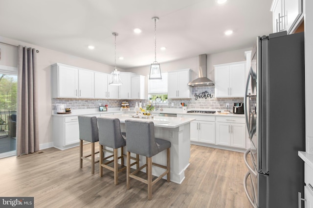 kitchen featuring white cabinets, wall chimney range hood, appliances with stainless steel finishes, and decorative backsplash
