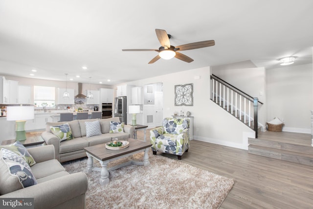 living room featuring light wood-type flooring, baseboards, recessed lighting, stairs, and ceiling fan