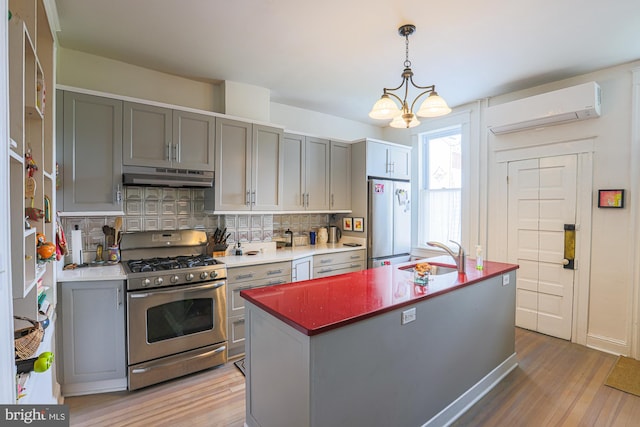 kitchen with stainless steel range with gas cooktop, freestanding refrigerator, a wall mounted AC, under cabinet range hood, and a sink