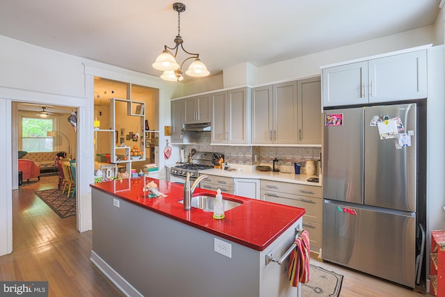 kitchen with appliances with stainless steel finishes, a sink, under cabinet range hood, light wood-type flooring, and tasteful backsplash