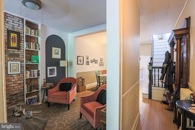 living area with wood finished floors, wainscoting, built in shelves, arched walkways, and ornamental molding
