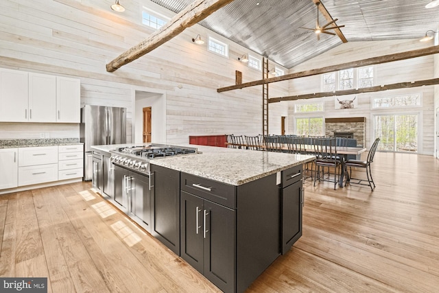 kitchen with white cabinets, stainless steel appliances, light stone counters, a ceiling fan, and high vaulted ceiling