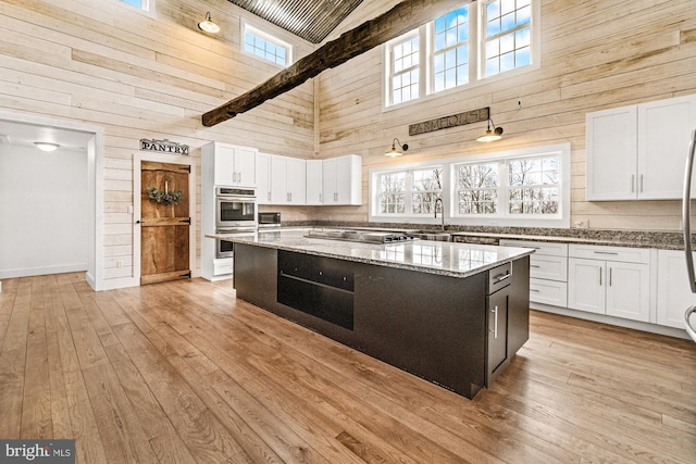 kitchen featuring white cabinets, a high ceiling, wood walls, and cooktop