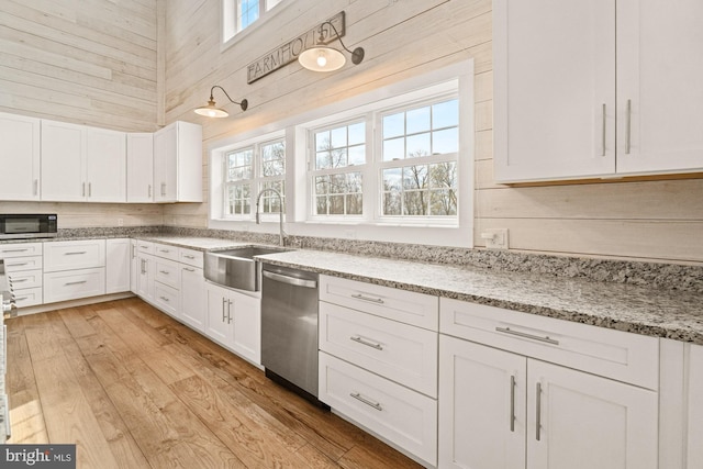 kitchen featuring light stone counters, a sink, wooden walls, stainless steel appliances, and white cabinets