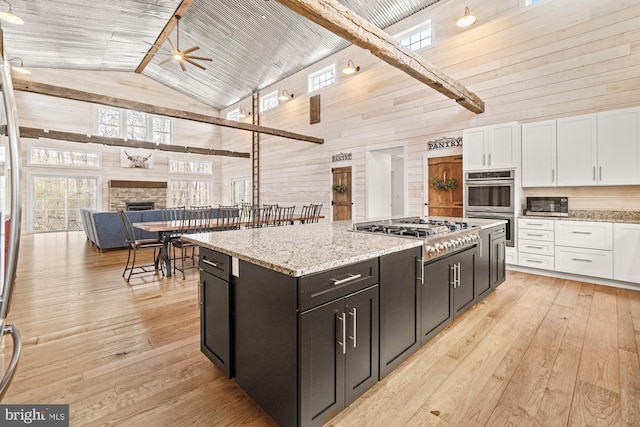 kitchen with white cabinets, plenty of natural light, stainless steel appliances, wooden walls, and high vaulted ceiling