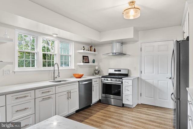 kitchen with wall chimney exhaust hood, stainless steel appliances, light wood finished floors, a sink, and open shelves
